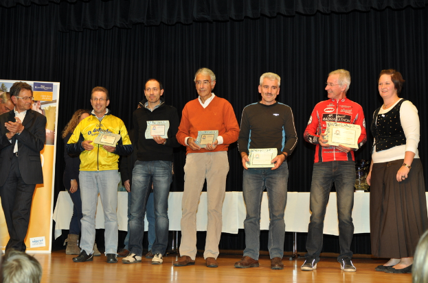 Eine Gruppe von Menschen steht auf einer Bühne und hält Zertifikate in den Händen, im Hintergrund eine Tafel, ein Tisch daneben und ein schwarzer Vorhang.