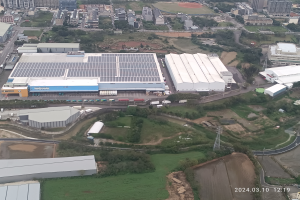 Eine Luftaufnahme eines großen Industriegebiets mit Gebäuden, Bäumen, Gras, Straßen, Fahrzeugen, Pfählen, Türmen und anderen Gegenständen, mit einem Wasserzeichen in der rechten unteren Ecke, das darauf hinweist, dass es die erste Solarstromanlage in Singapur ist.