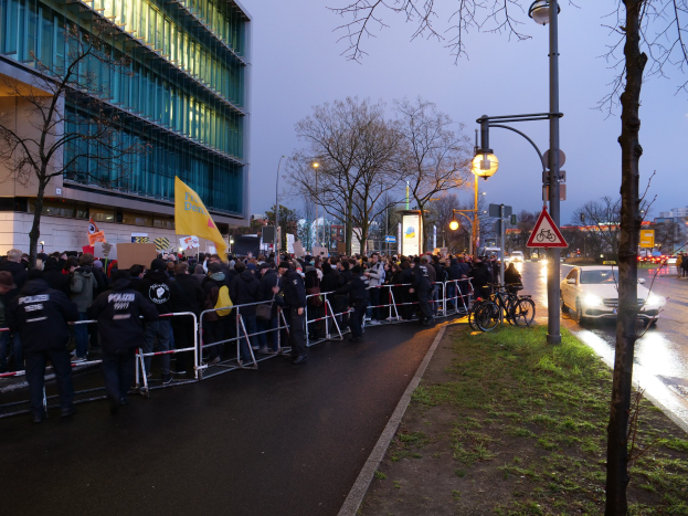 Große Gruppe von Menschen vor einem Gebäude mit Barrikaden, Schildern, Fahrrädern und Bäumen, was auf eine Protestaktion in Berlin hinweist.