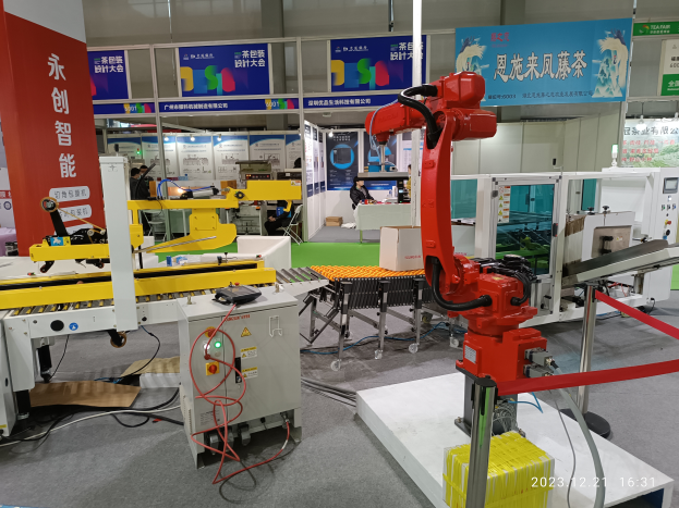 Eine Gruppe von Robotern auf einem Tisch umgeben von Maschinen und Kabeln, mit ein paar Menschen im Hintergrund in einer Fabrikeinrichtung.