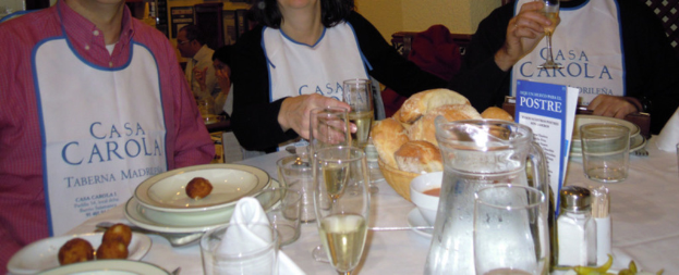 Personen an Tischen mit Tellern, Besteck, Gläsern und einem Brotkorb, mit einer Werbung im Hintergrund.