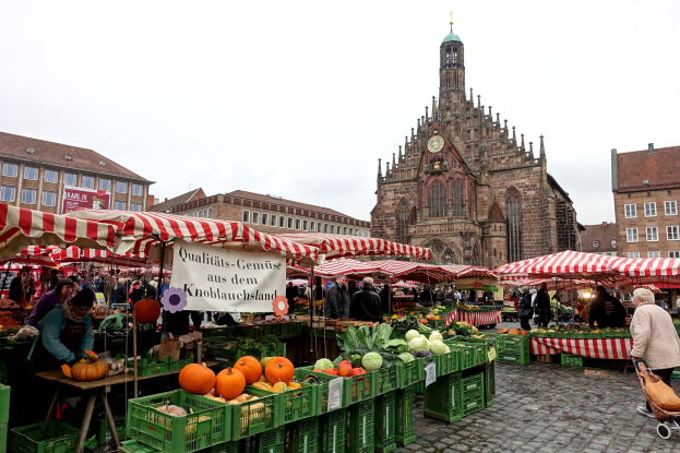 Ein belebter Markt in Nürnberg, Deutschland, mit Obst, Gemüse, Zelten, Menschen und Gebäuden mit einem Uhrenturm im Hintergrund.