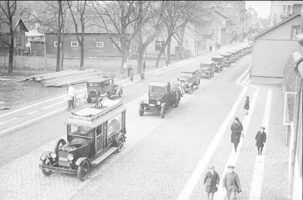 Schwarz-weißes Straßenbild in Berlin aus den 1930er-1940er Jahren, das Autos, Fußgänger, Gebäude mit Fenstern, Bäume und einen klaren Himmel zeigt.