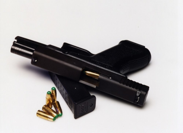 Schwarze Handfeuerwaffe mit einem Magazin und Patronen auf einer weißen Oberfläche.