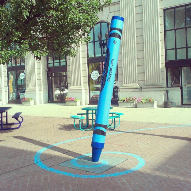 Ein Gebäude mit Türen in der Mitte, einem Baum im oberen linken Eck und Bänken in der Mitte.