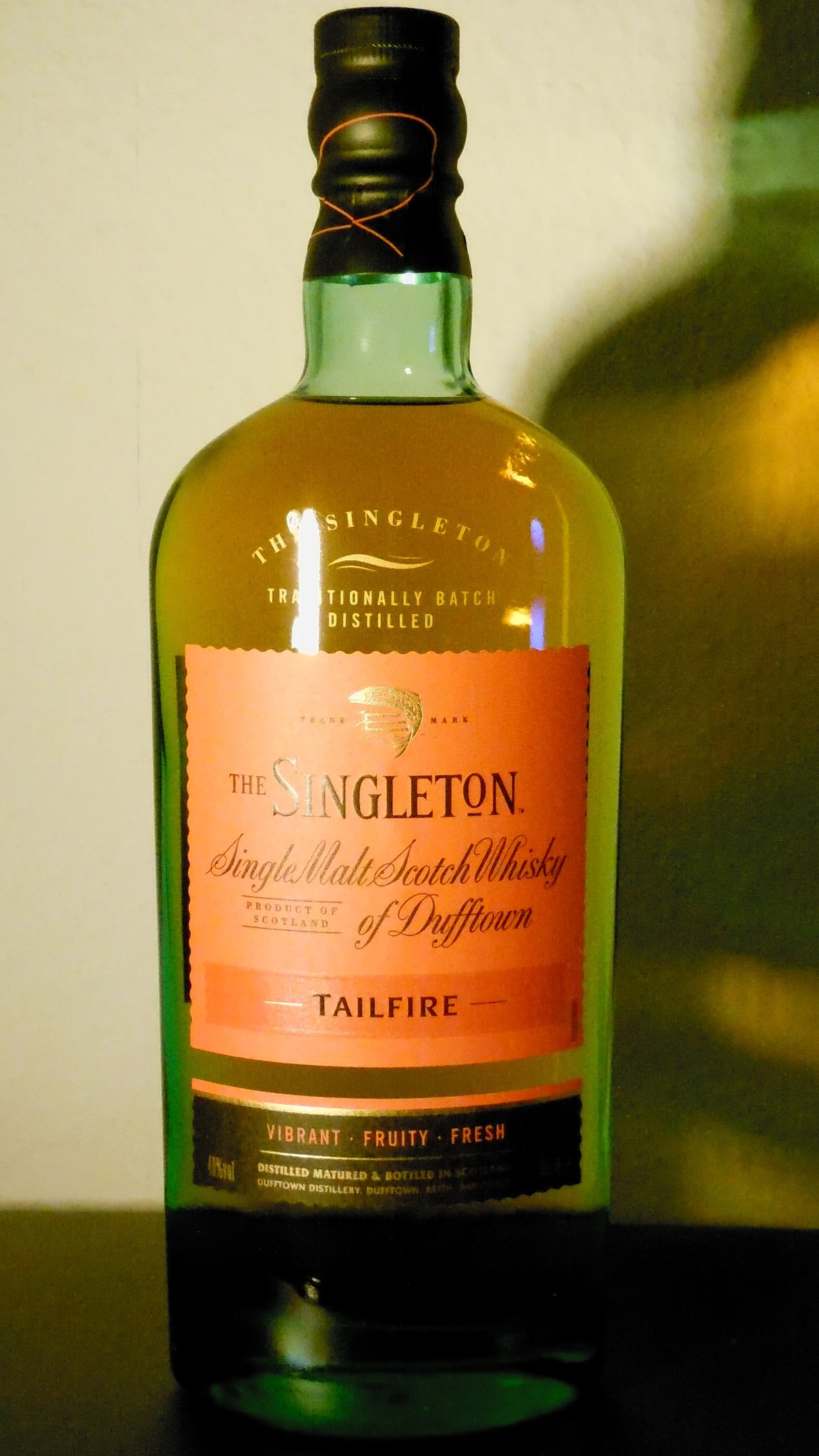 Tiefe bernsteinfarbene Flasche Singleton of Dufftown Tailfire Single Malt Scotch Whisky mit einem schwarzen Etikett, das ein Wappen mit einem Löwen und einer Burg zeigt.