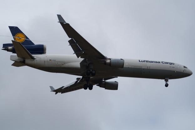 Ein Lufthansa Cargo Boeing 777-300ER im Flug, mit ausgefahrenen Flügeln und laufenden Triebwerken, mit sichtbarem Text auf der Rumpfseite vor einem bewölkten Himmel.