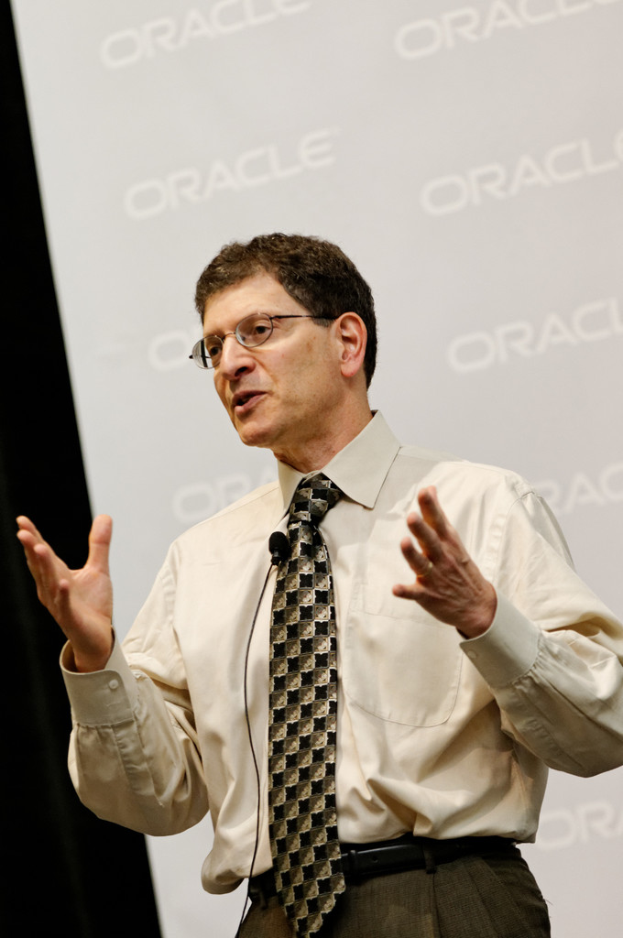 Eine Person steht vor einer Sponsorwand und trägt Kleidung und Brille.