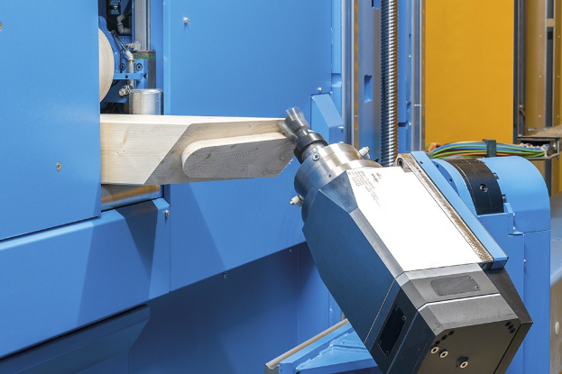 CNC-Fräsmaschine schneidet ein Holzstück in einer Fabrikumgebung, umgeben von Kabeln und Geräten mit einer Wand im Hintergrund.