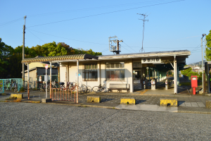 Ein Bahnhof mit Fahrrädern davor, eine Straße darunter und Häusern, Bäumen, Polen, Drähten und einem klaren blauen Himmel im Hintergrund.