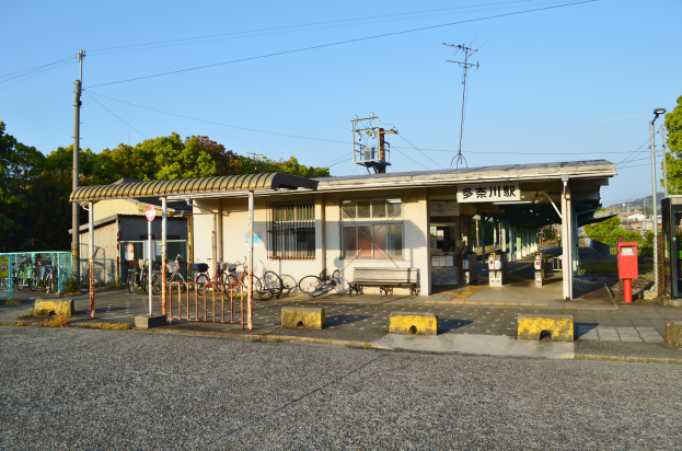 Ein Bahnhof mit Fahrrädern davor, eine Straße darunter und Häusern, Bäumen, Polen, Drähten und einem klaren blauen Himmel im Hintergrund.