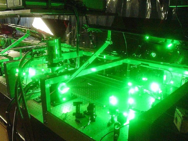 Eine Lasermaschine auf einem Tisch, die grünes Licht abstrahlt, mit sichtbaren Komponenten und angeschlossenen Kabeln.