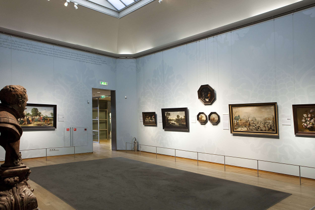 Ein prächtiger Museumsraum mit einer Statue links, einem Teppichboden, Fotorahmen an den Wänden, einer Glasdecke mit Lampen und Türen im Hintergrund.