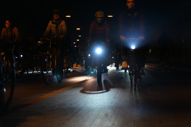 Eine Gruppe von Menschen, die nachts mit Fahrrädern auf einer Stadtstraße fahren und Helme tragen, beleuchtet von Stadtlichtern.