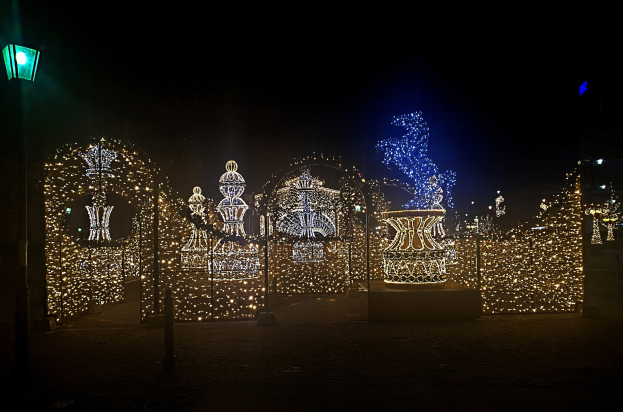 Eine nächtliche Parkszene mit Weihnachtslichtern in einem dekorativen Muster, beleuchtet von einer Straßenlaterne auf der linken Seite.
