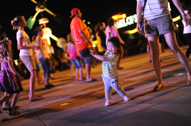 Ein Kind tanzt auf einem Boden mit unscharfen Figuren von tanzenden Menschen im Hintergrund.