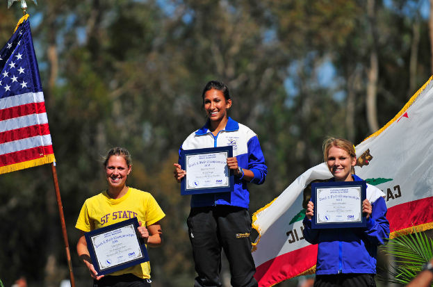 Drei Frauen stehen und halten Zertifikate, mit Flaggen und Bäumen im Hintergrund.