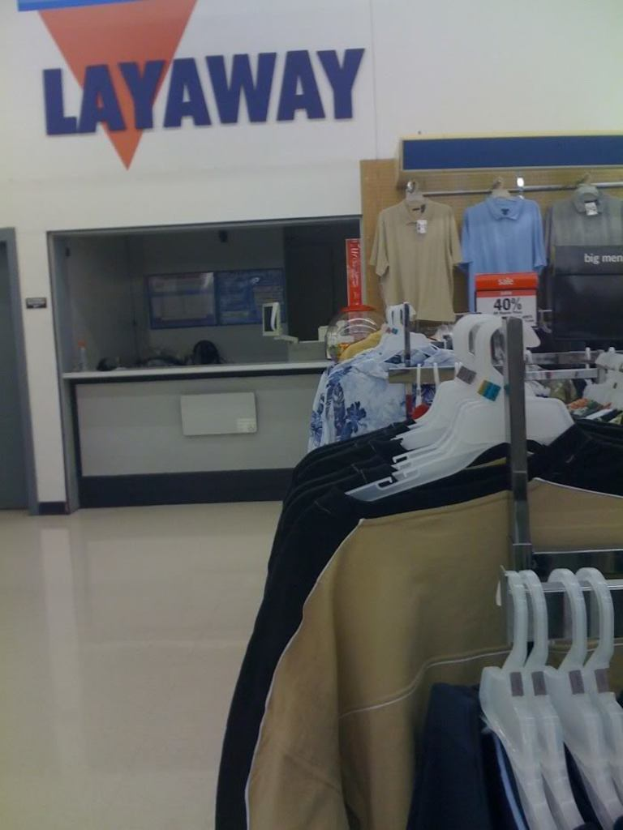 Ein Innenblick in ein Geschäft mit Kleidung an Ständern, einem Tisch und einer Preistafel.