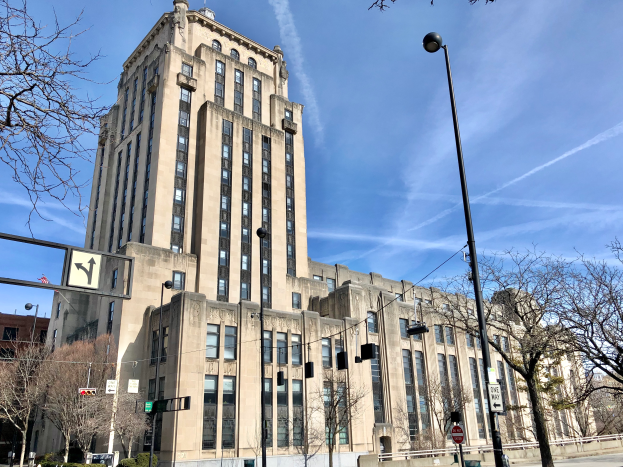 Das University of Illinois Medical Center, ein großes Gebäude mit vielen Fenstern, ist von Straßenmasten, Straßenlaternen, Verkehrsampeln, Schildern, Kraftfahrzeugen, Büschen, Bäumen und einer bewölkten Himmel umgeben.