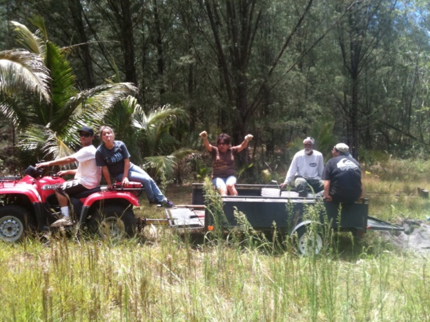 Eine Gruppe von Menschen sitzt auf einem Traktor mit einer Person, die ihn fährt, mit Bäumen im Hintergrund.