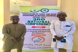 Zwei Männer stehen nebeneinander vor einer Fahne mit der Aufschrift "3. Nationaler Kongress" mit einer Säule und Deckenbeleuchtung im Hintergrund, datiert 2023.