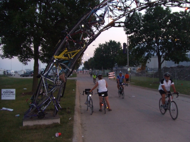 Eine Gruppe von Menschen, die auf einer Straße mit grünem Gras auf der linken Seite fahren, umgeben von Bäumen und Fahrzeugen.