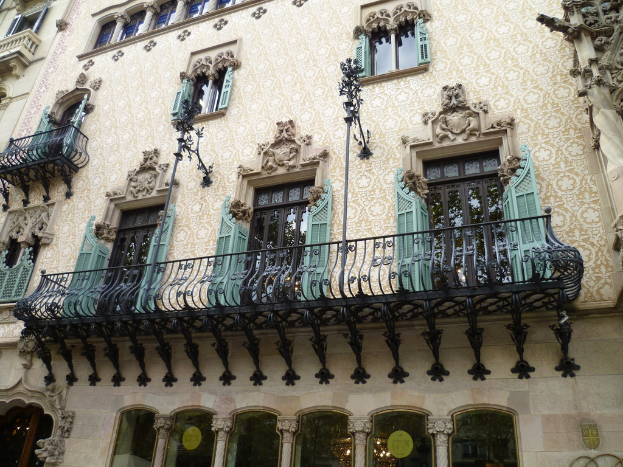 Ein Gebäude mit Fenstern und Balkonen, das Stangen, detaillierte Wandverzierungen und eine unten sichtbare Pendelleuchte aufweist.