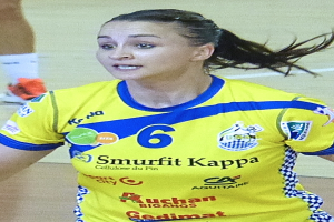 Eine Frau in einer gelben und blauen Uniform spielt Volleyball, wobei ein menschlicher Unterschenkel im Hintergrund zu sehen ist.