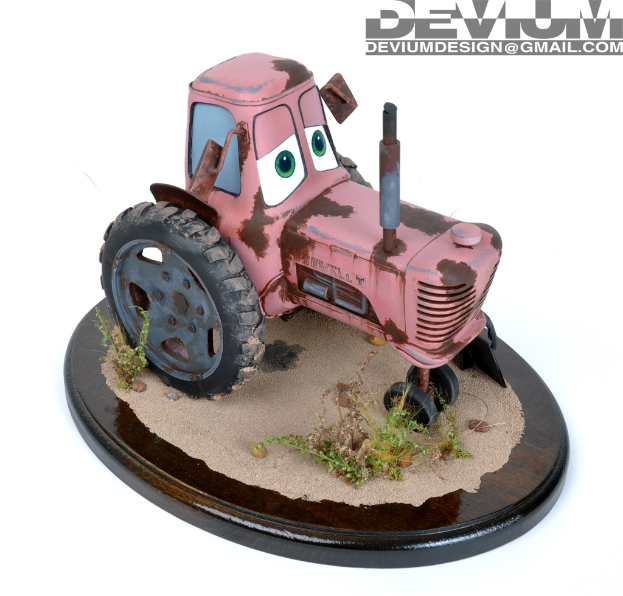 Ein Spielzeugtraktor steht auf einer braunen, sandigen Oberfläche mit spärlicher Vegetation, und ein Wasserzeichen ist in der oberen rechten Ecke sichtbar.