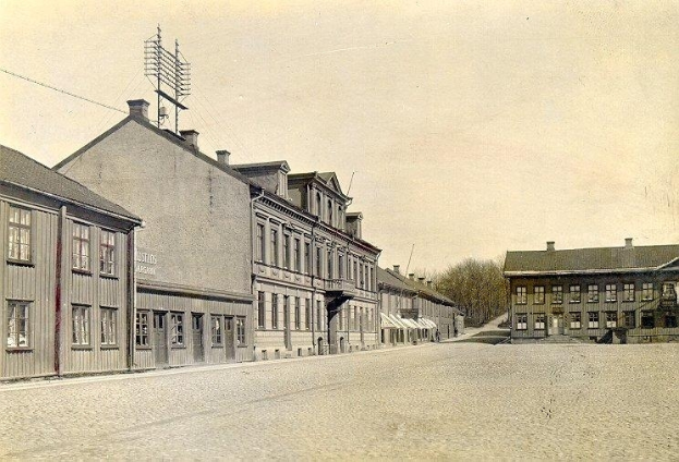 Ein altes Schwarz-Weiß-Foto einer Stadtstraße mit Gebäuden, Fenstern, Bäumen, Pfählen, Drähten und einem Himmel im Hintergrund, mit dem Text "Stadtstraße in Stadtström" unten.