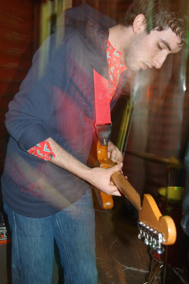 Ein Gemälde eines jungen Jungen in einem weißen Hemd, der konzentriert eine Gitarre spielt, die Augen geschlossen und die Finger auf dem Griffbrett.