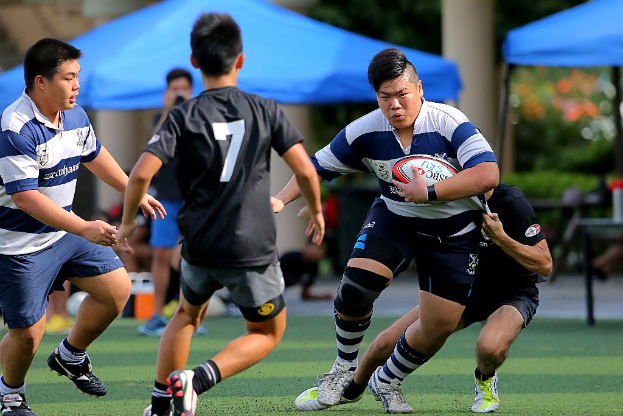 Vier Personen gehen, eine hält einen Ball, mit blauen Zelten in der Ferne.