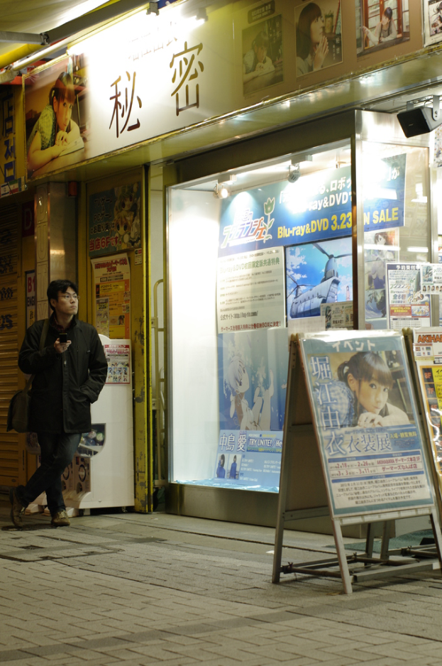 Ein Mann steht mit einem Mobiltelefon in der Hand, trägt eine Tasche und hält Schilder mit Text, Geschäfte, Lampen und Papiere mit Text im Hintergrund.