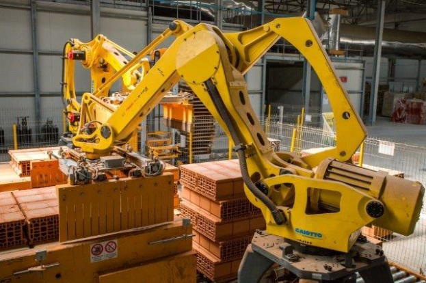 Großes industrielles Lager mit gestapelten Kisten, Überkopfkranen, Zaun, Pfählen und einer fernen Wand in einer Fertigungsumgebung.