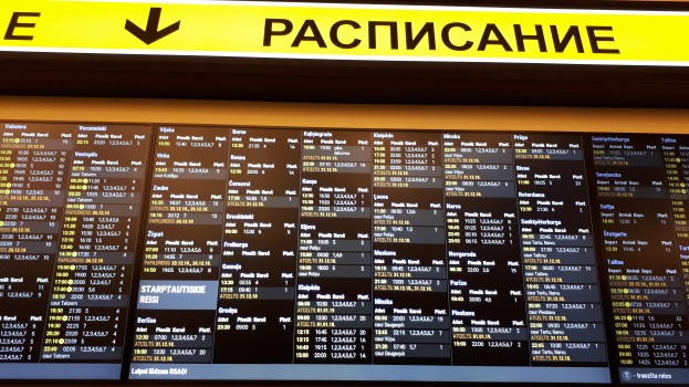 Ein Abflugtafel am Airport voller Text und Zahlen, die Fluginformationen anzeigen, mit einem gelben Schild darüber.