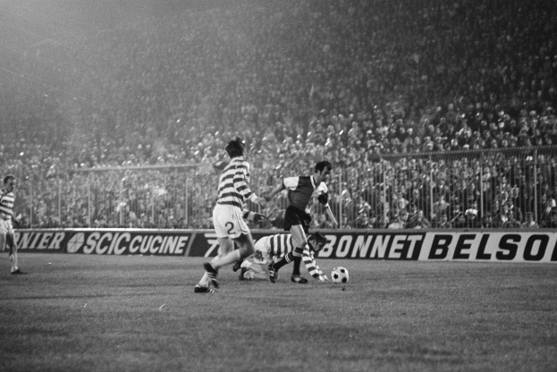 Schwarzes und weißes Foto von Männern, die auf einem Feld Fußball spielen, mit Zuschauern auf den Tribünen und einem Banner mit der Aufschrift "Celtic v West Bromwich Albion - FA Cup Third Round."