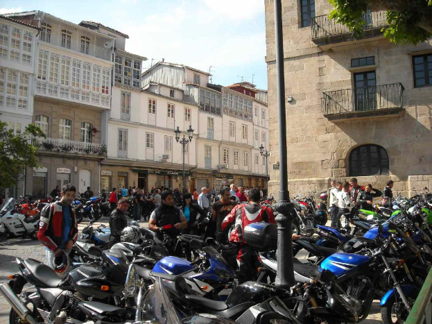 Ein cremefarbenes Gebäude mit zahlreichen Fenstern, angrenzend an ein Backsteingebäude mit einer Metallbalustrade, mit mehreren geparkten Fahrrädern und Menschen, die davor diskutieren.