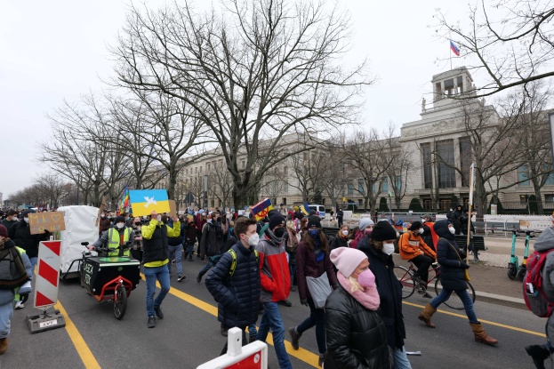 Eine große Gruppe von Menschen marschiert auf einer Demonstration in Washington, D.C. am 21. Januar 2020 mit Schildern und Transparenten, einige fahren Fahrräder, mit Bäumen und einem klaren blauen Himmel im Hintergrund.