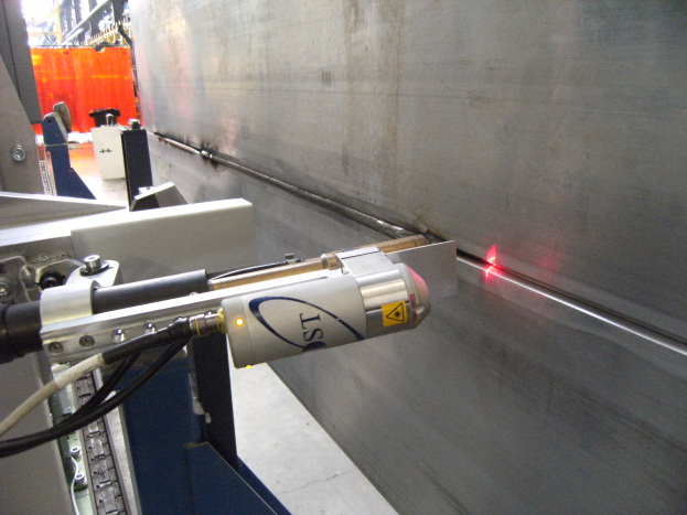 Eine Laser-Schneidemaschine in einer Fabrik strahlt helles Licht aus und erhellt die Umgebung mit einer Wand auf der rechten Seite und einigen Gegenständen im Hintergrund.