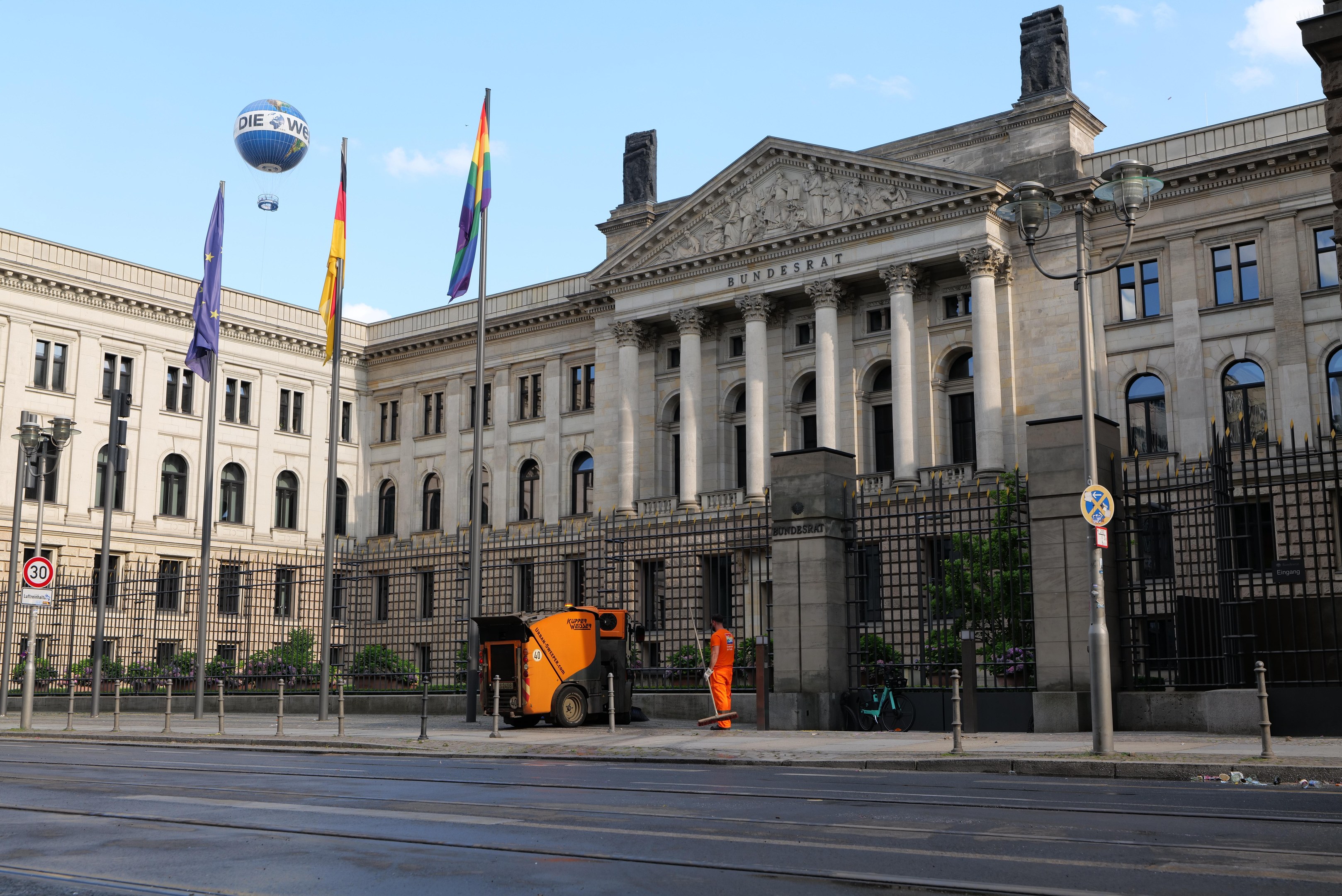 Großes modernes Gebäude mit vielen Fenstern, als Bundestag in Berlin, Deutschland identifiziert, umgeben von Straßeninfrastruktur, Fußgängern und Bäumen unter einem bewölkten Himmel.