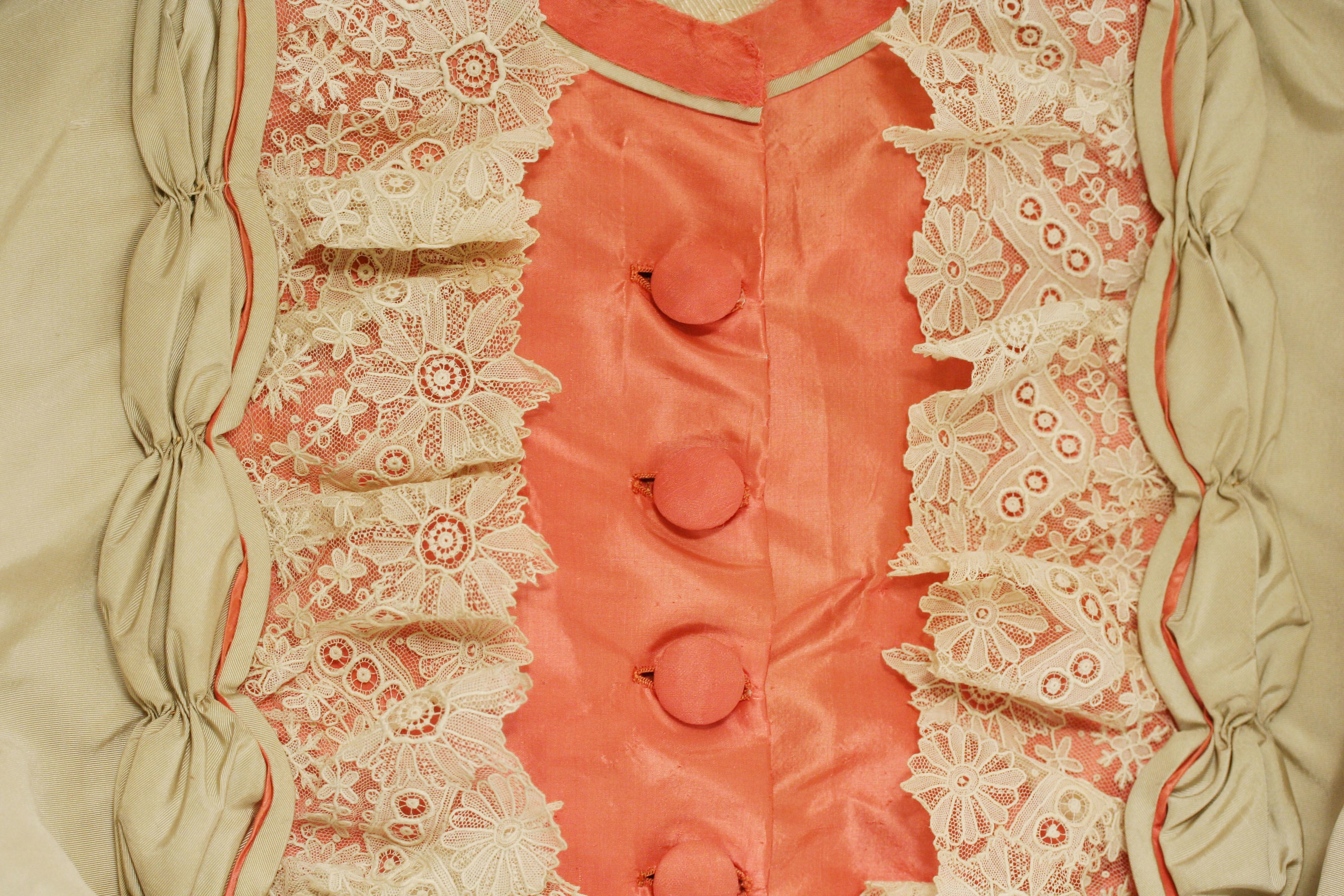 Nahaufnahme eines rosafarbenen und cremefarbenen Kleides mit weißer Spitze und vorderen Knöpfen, das eine klassische und elegante Gestaltung aufweist.