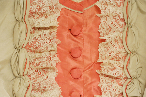 Nahaufnahme eines rosafarbenen und cremefarbenen Kleides mit weißer Spitze und vorderen Knöpfen, das eine klassische und elegante Gestaltung aufweist.