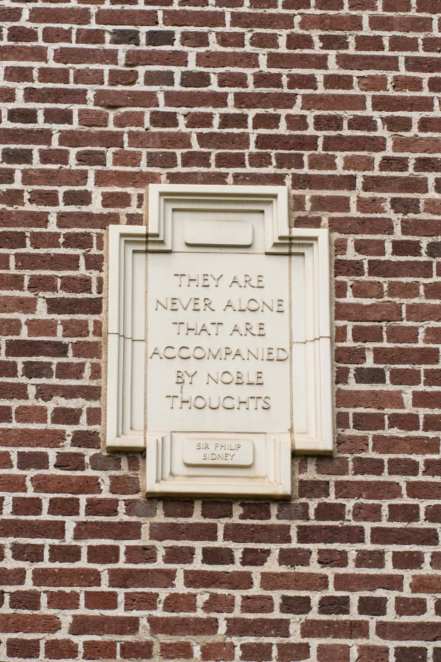 Eine Steinplatte auf einer Backsteinwand mit der Inschrift "Sie sind nie allein, die von edlen Gedanken begleitet sind" in fetter Schrift.