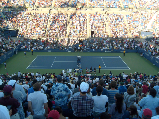 Eine große Menschenmenge in einem Stadion schaut einem Tennismatch zu, das eine elektrisierende Atmosphäre schafft.