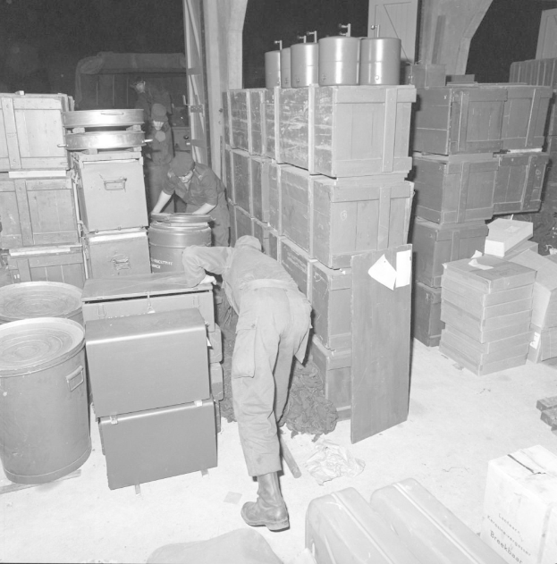 Schwarz-weiß-Bild von Männern, die in einem Lager arbeiten, umgeben von Kisten und Containern.