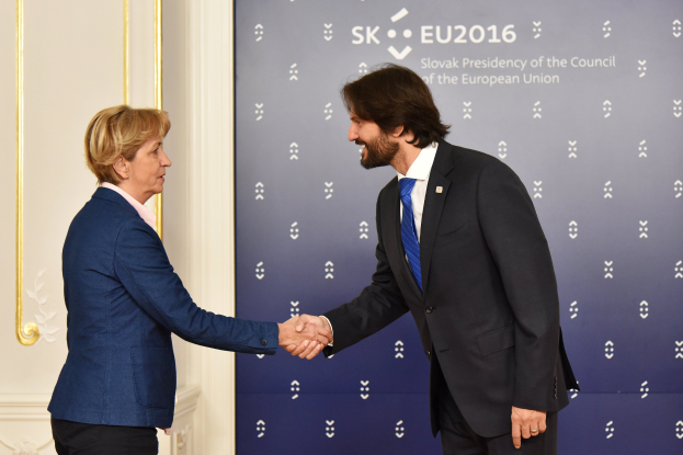 Bundeskanzlerin Angela Merkel und Bundeskanzler Joachim Gauck schütteln sich vor einer Wand mit einem "EU-Gipfel"-Schild und einer Tür im Hintergrund die Hände, beide lächeln.