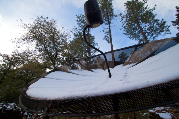 Eine Schüsselantenne mit Schnee darauf, mit ein paar Bäumen im Hintergrund und einem klaren Himmel.
