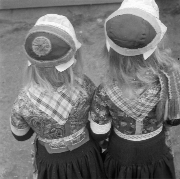 Zwei junge Mädchen in traditionellen bayerischen Kleidern und Hüten stehen nebeneinander vor einer Wand und werden auf einem Schwarz-Weiß-Foto abgebildet.