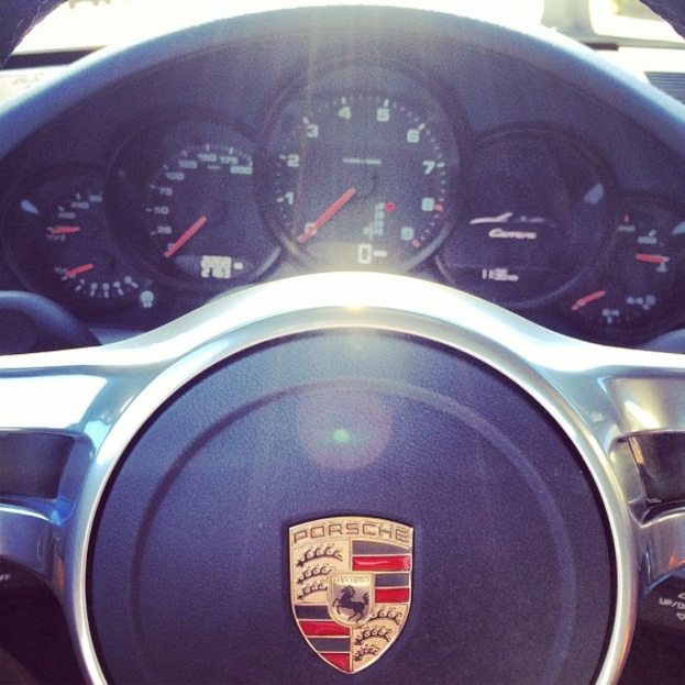 Ein Nahaufnahme-Bild eines Porsche-Auto-Dashboards mit Tacho und Lenkrad.