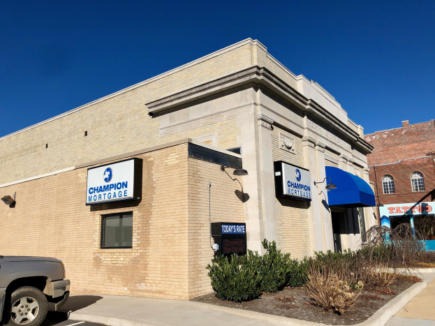 Bauen mit "Champion Mortgage, Inc."-Schilder, einem geparkten Auto, Pflanzen, Bäumen und einem bewölkten Himmel.